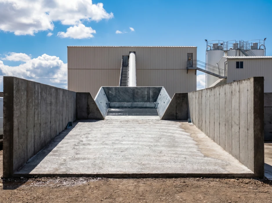 Aire de réception industrielle extérieure en béton brut, flanquée de murs de soutènement