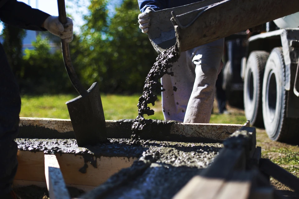Chantier extérieur avec ouvrier versant du béton frais depuis une benne dans un coffrage en bois