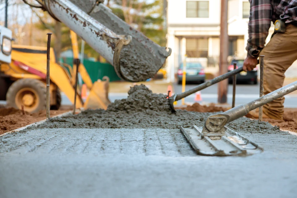Chantier extérieur avec ouvrier versant du béton frais depuis une benne dans un coffrage en bois