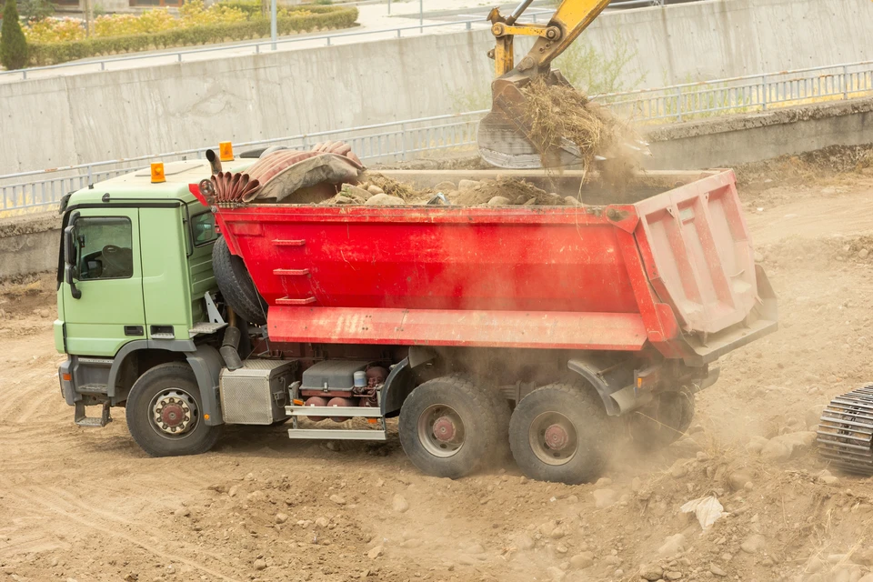 Chantier extérieur avec ouvrier versant du béton frais depuis une benne dans un coffrage en bois